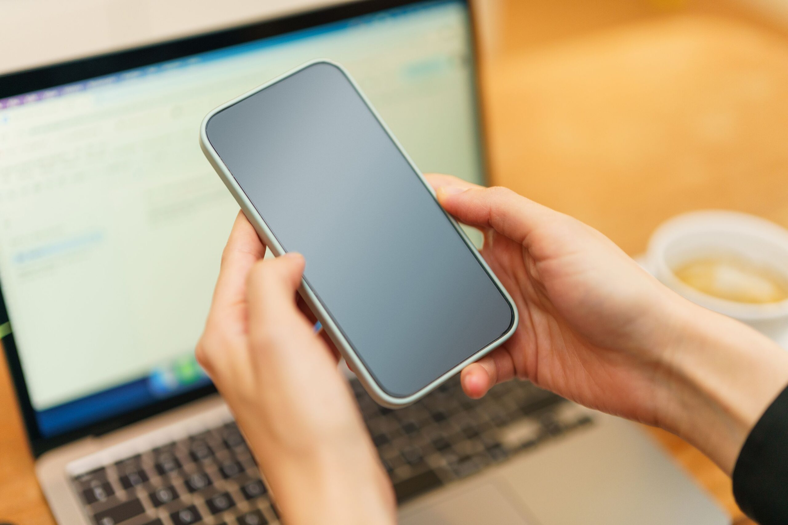 Persona sosteniendo un smartphone frente a un portátil abierto, representando la sincronización entre dispositivos y la accesibilidad de los marcadores en iOS, Android y escritorio.