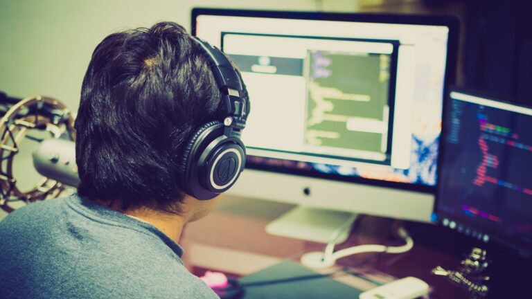 Programador concentrado trabajando en un entorno de desarrollo profesional con configuración de monitores duales.