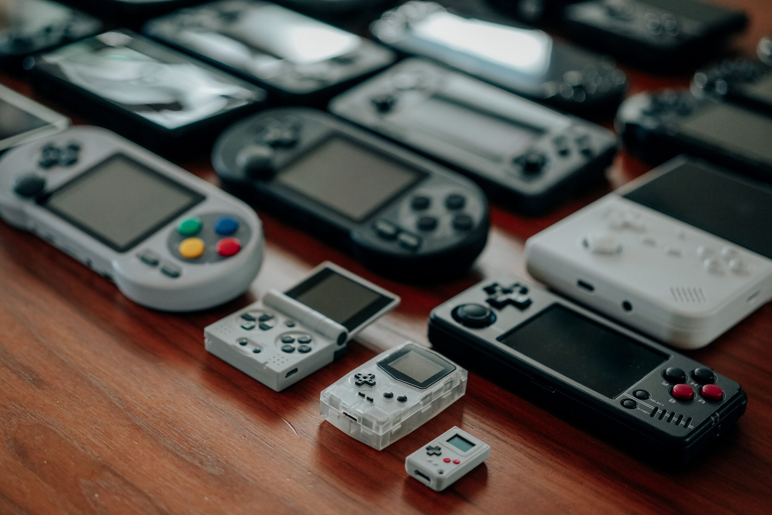 Variedad de consolas portátiles retro de diferentes épocas dispuestas sobre una mesa de madera.