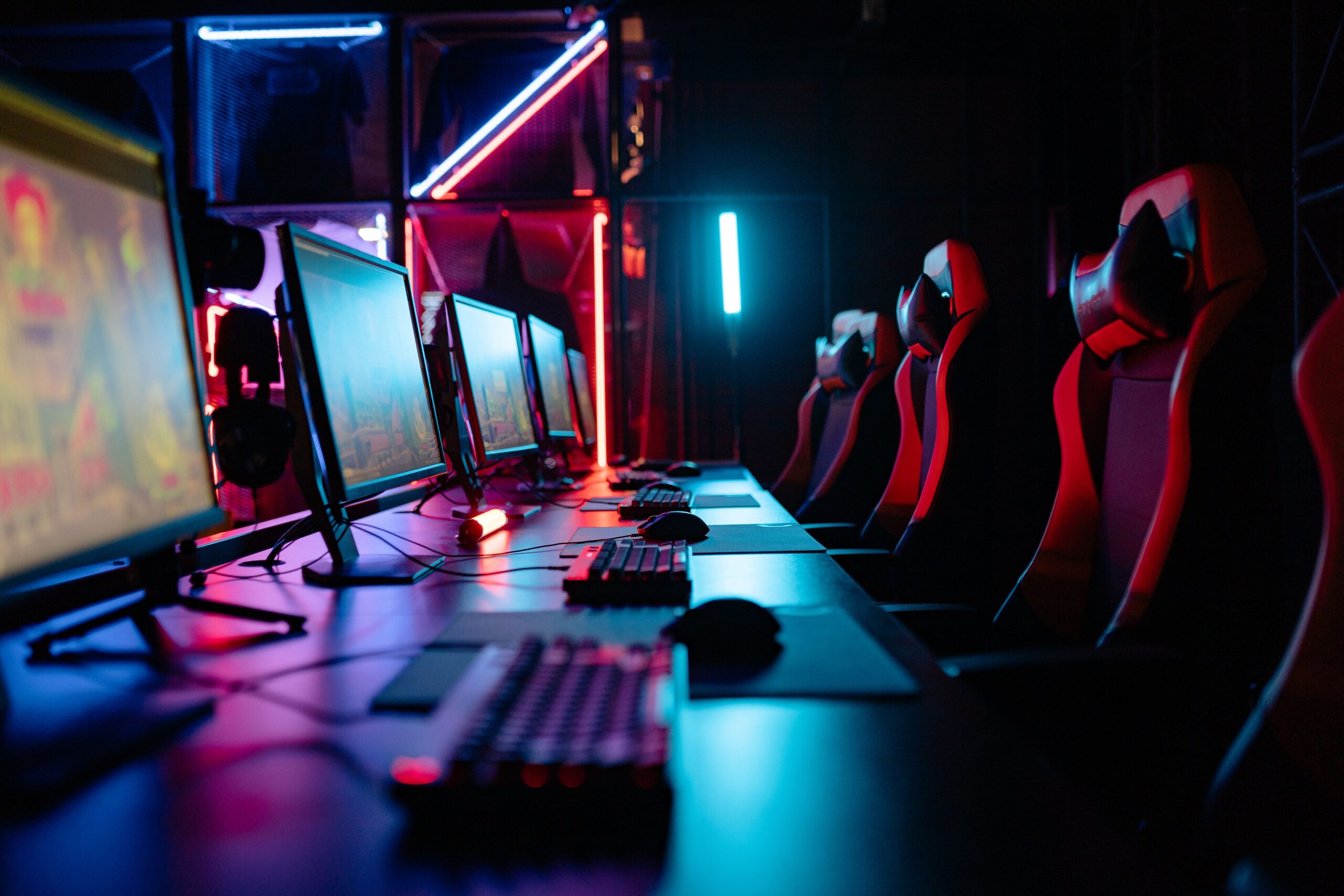 Habitación de gaming profesional y competitiva con luces de neón, múltiples pantallas y sillas ergonómicas.
