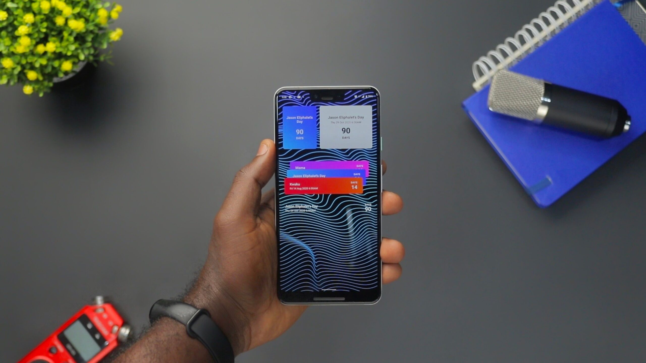 Mano sosteniendo un smartphone con notificaciones en pantalla sobre un escritorio