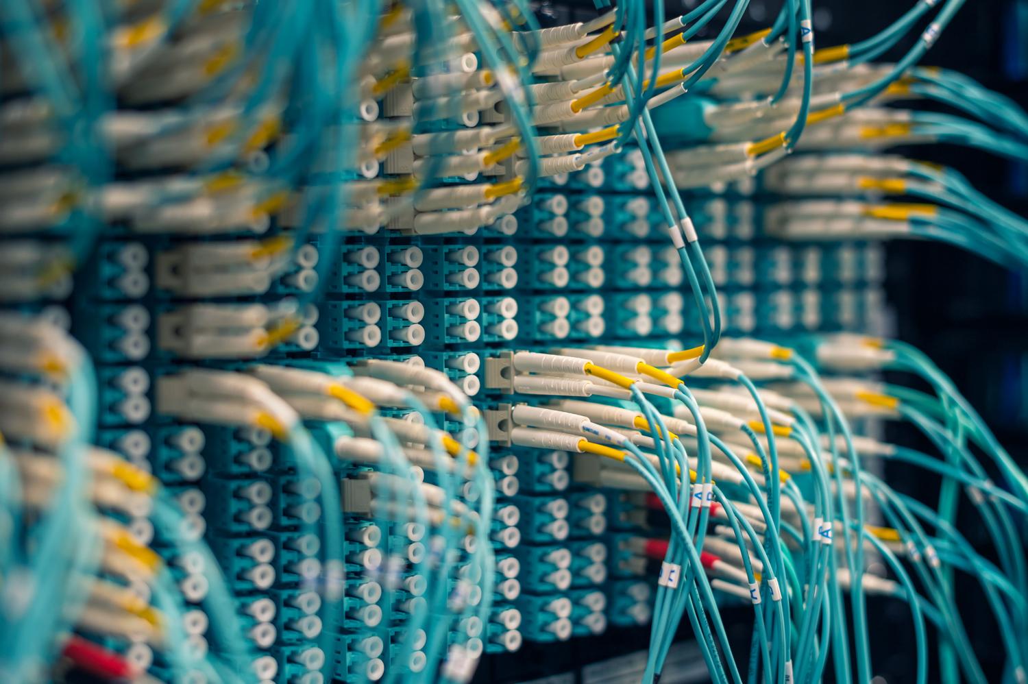 Detalle de un panel de conexiones de fibra óptica con cables aqua, sirviendo como metáfora visual de los endpoints y la transmisión inmediata de información.