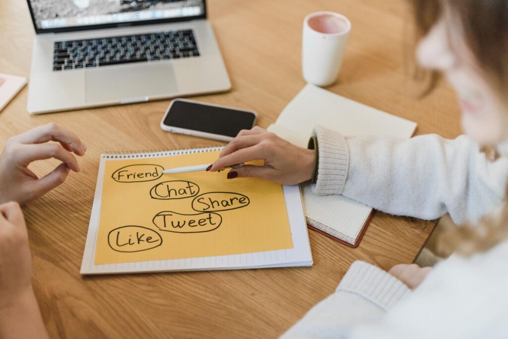 Dos mujeres planificando la estrategia de marketing en redes sociales con un portátil y notas en un escritorio.