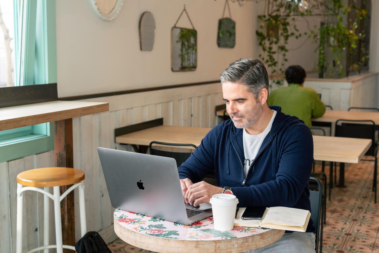 Hombre utilizando un ordenador portátil en una cafetería, ilustrando el acceso remoto a archivos desde fuera de casa.