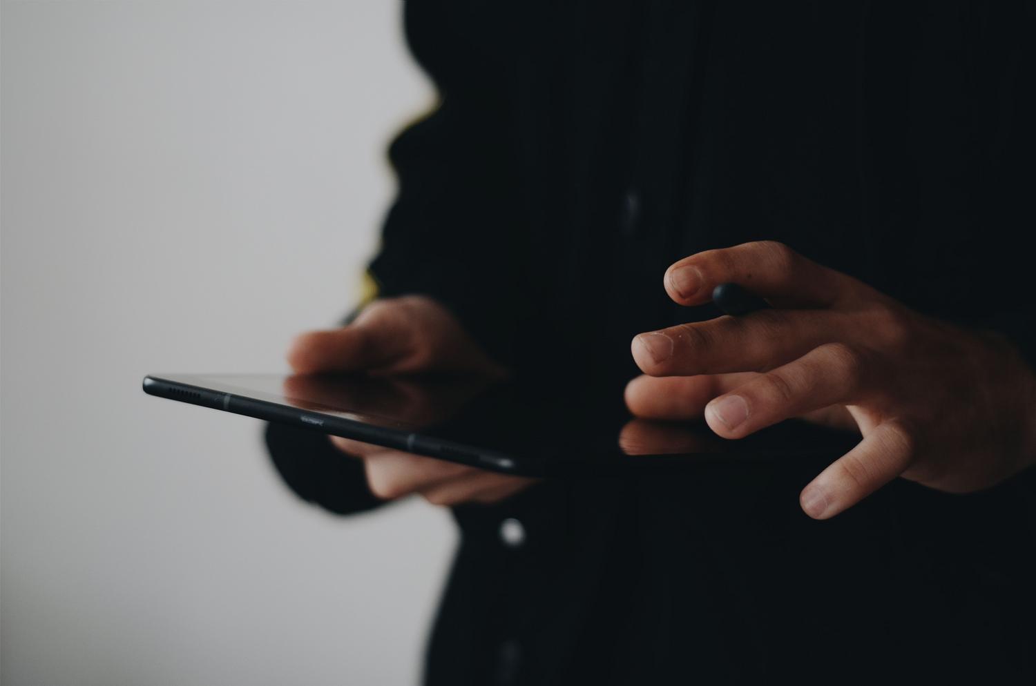 Primer plano de manos interactuando con la pantalla de una tablet, evocando el gesto de búsqueda de Spotlight.