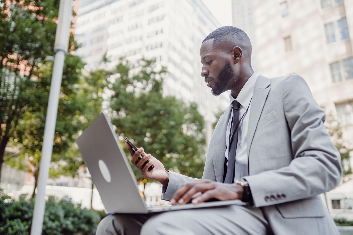 Profesional de negocios utilizando simultáneamente un ordenador portátil y un teléfono móvil, representando la eficiencia operativa de un empleado digital.