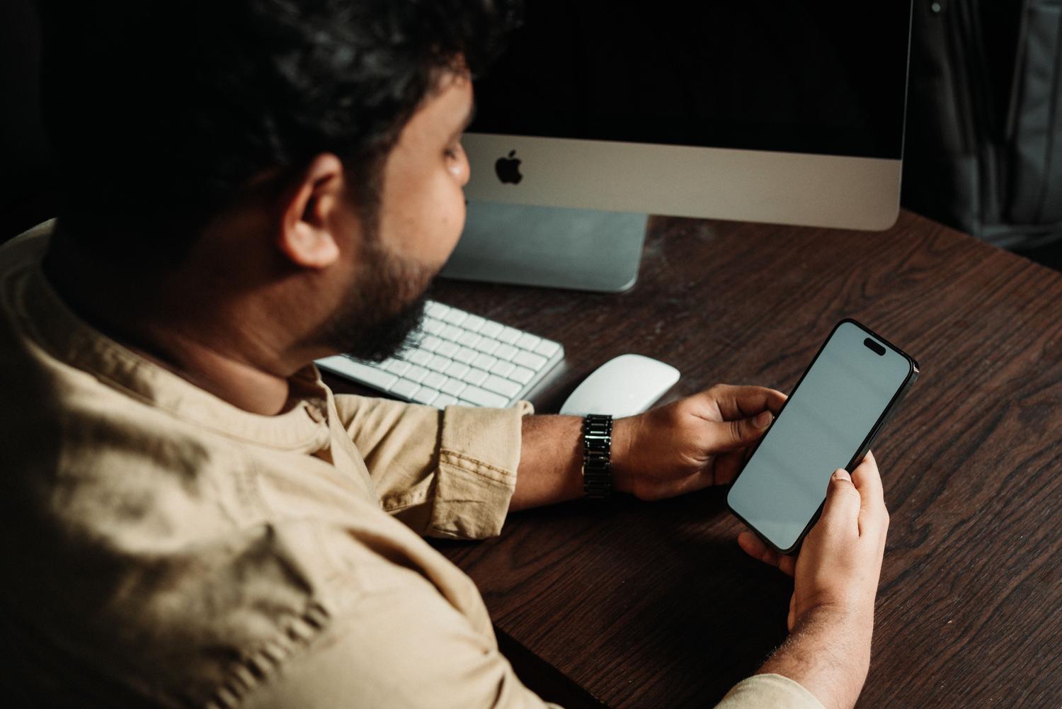 Empleado de oficina revisando notificaciones en su smartphone mientras trabaja en su escritorio, ilustrando la gestión diaria de chats de empresa.