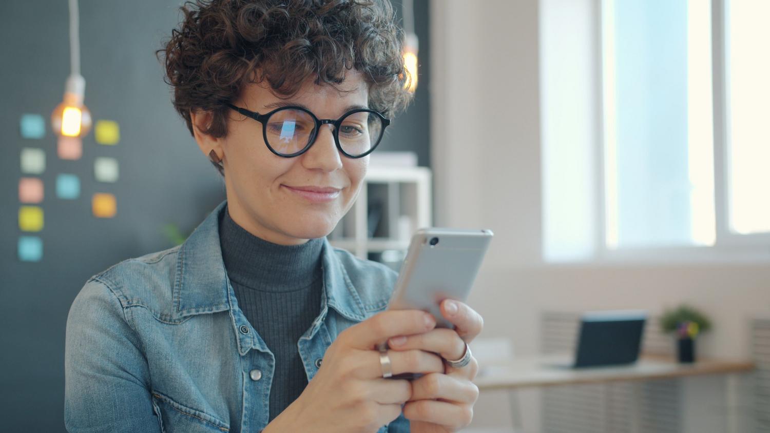 Mujer profesional sonriente utilizando un smartphone en una oficina moderna, representando la gestión de WhatsApp Business.