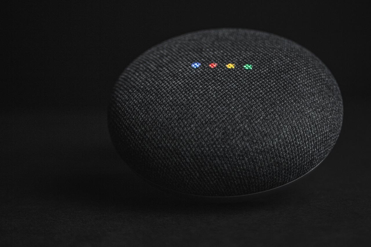Dispositivo de asistente digital compacto sobre una superficie blanca, símbolo de la gestión de audio mediante IA