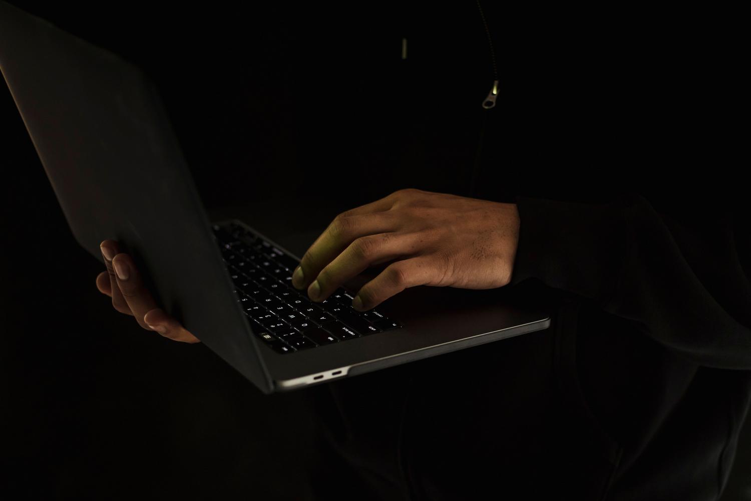 Usuario anónimo con portátil en un entorno oscuro, ilustrando el concepto de 'máscara digital' y el uso de alias para no revelar el email real.