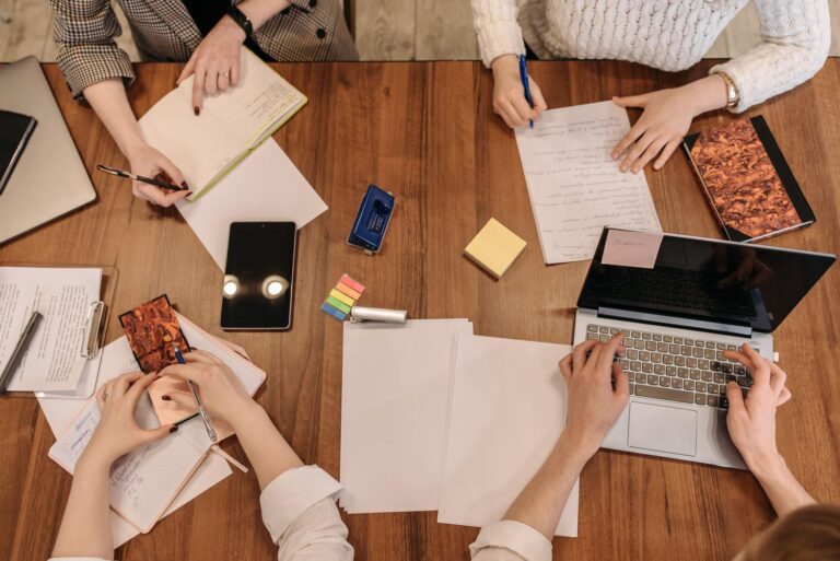 Equipo de trabajo colaborando en una mesa de madera con portátiles y libretas, representando la organización y el trabajo en equipo.