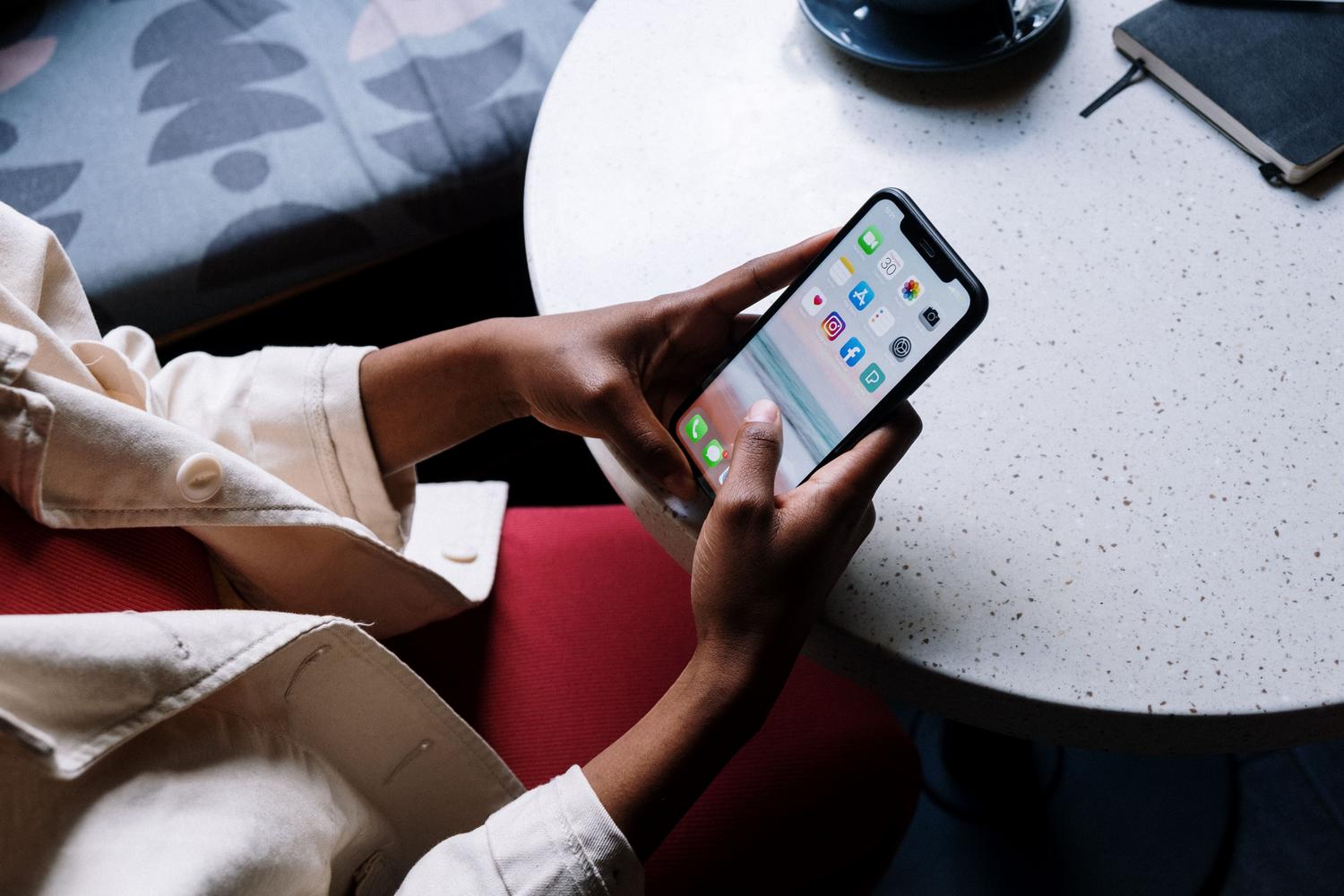 Manos sosteniendo un smartphone junto a una taza de café en una mesa de cafetería