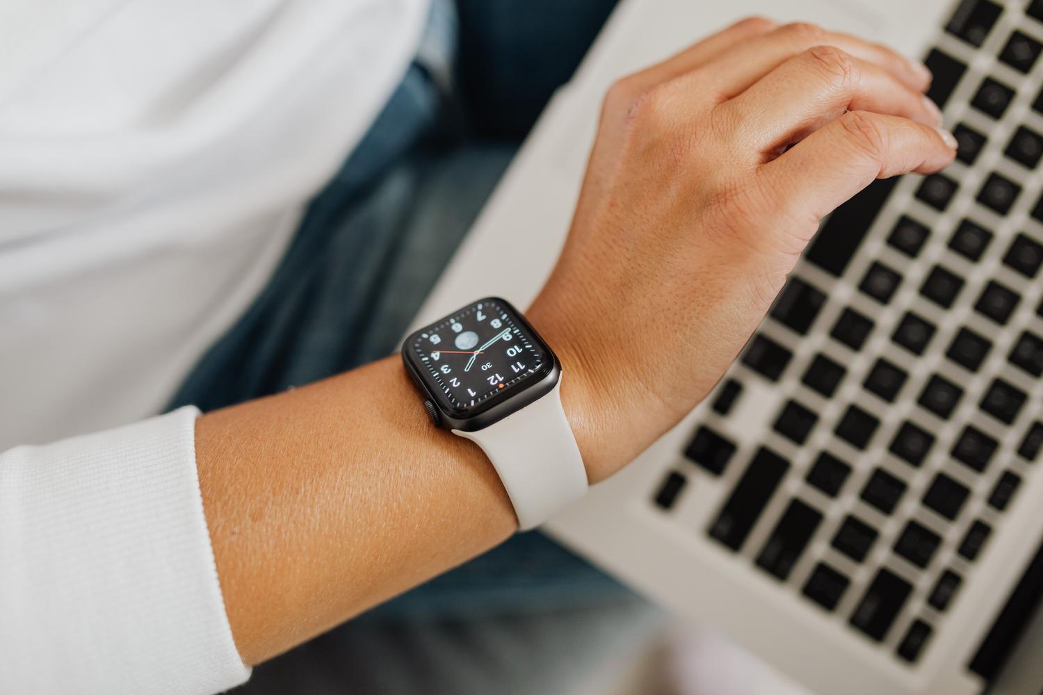 Persona utilizando un Apple Watch mientras trabaja con un ordenador portátil, representando la integración tecnológica.