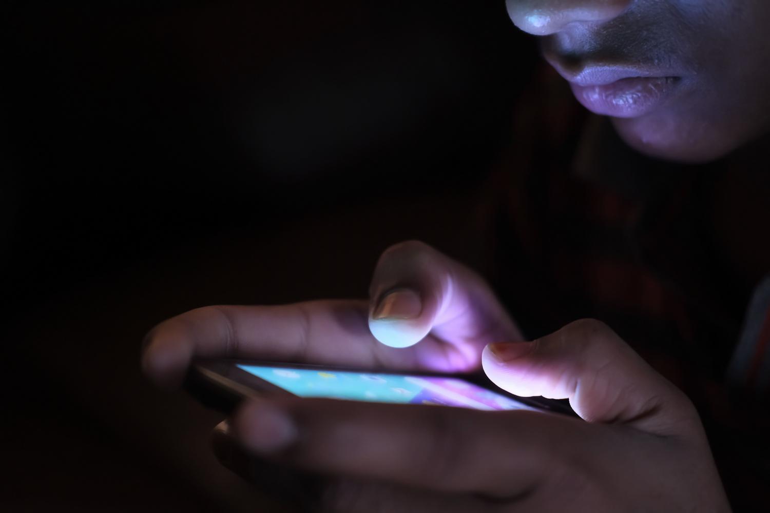 Persona utilizando un smartphone en un entorno oscuro, ilustrando el uso del dispositivo y el ahorro de energía