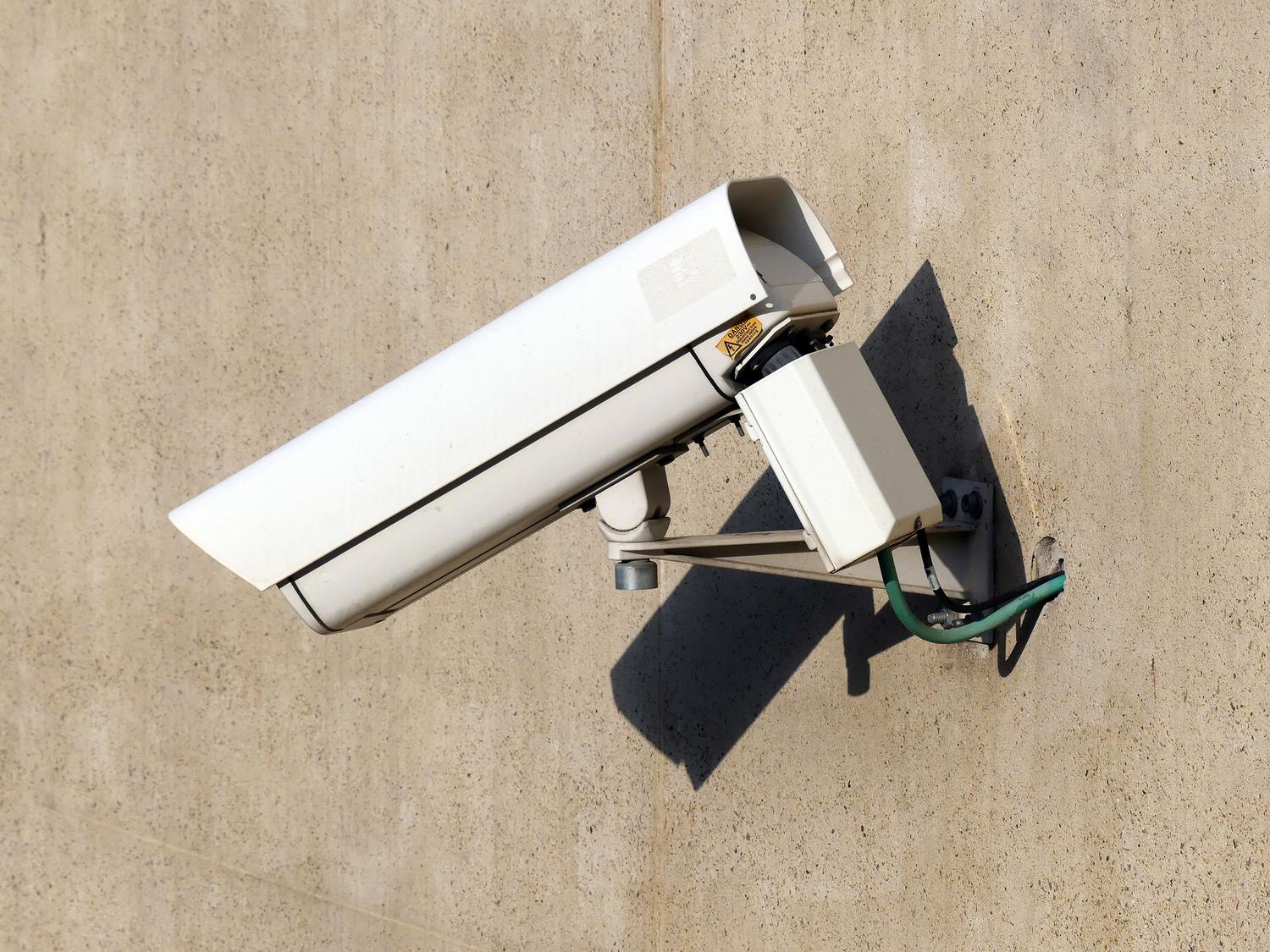 Cámara de seguridad blanca montada en una pared exterior bajo la luz del sol para la detección de personas.