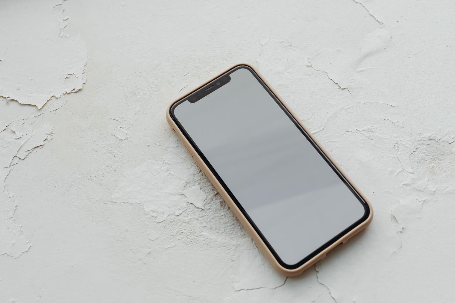 Teléfono inteligente con pantalla apagada sobre una superficie texturizada blanca, reflejando un diseño industrial y minimalista.