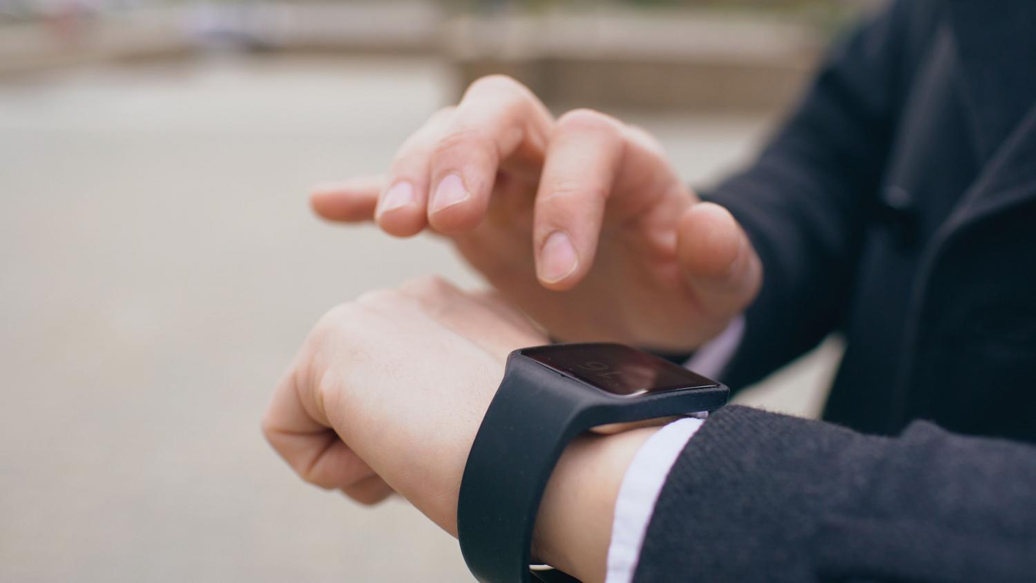 Persona interactuando con la pantalla de su smartwatch en un entorno exterior, simulando la activación de Shazam para reconocer música.
