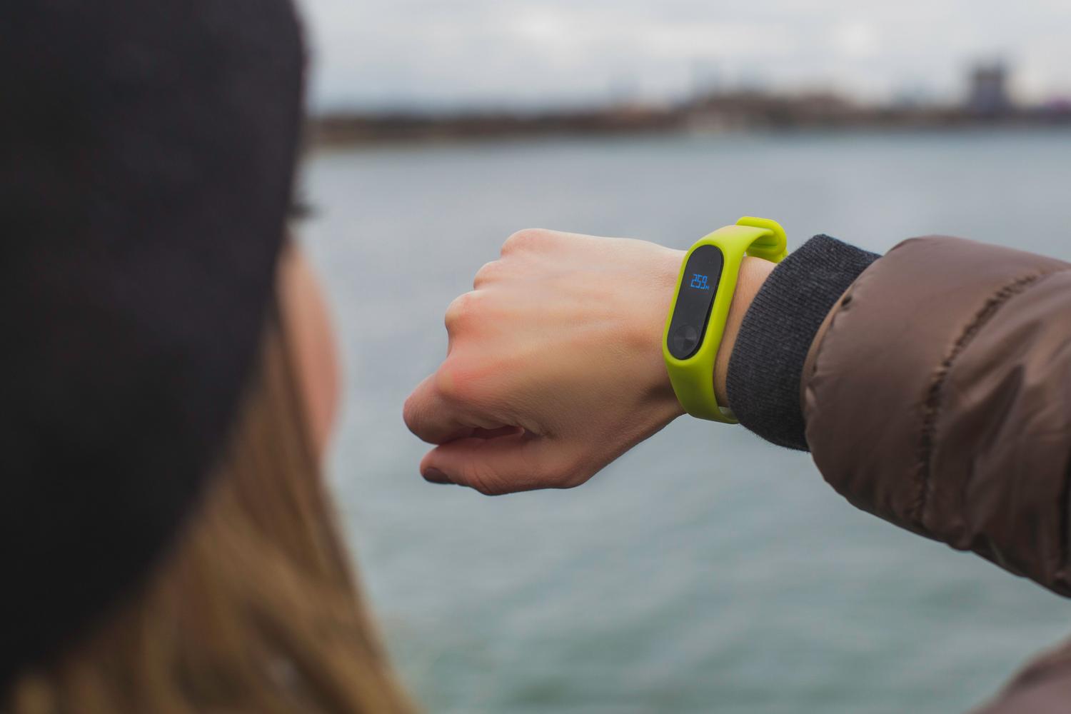 Mujer consultando su reloj inteligente al aire libre junto a un lago, representando la identificación de canciones mientras se pasea.