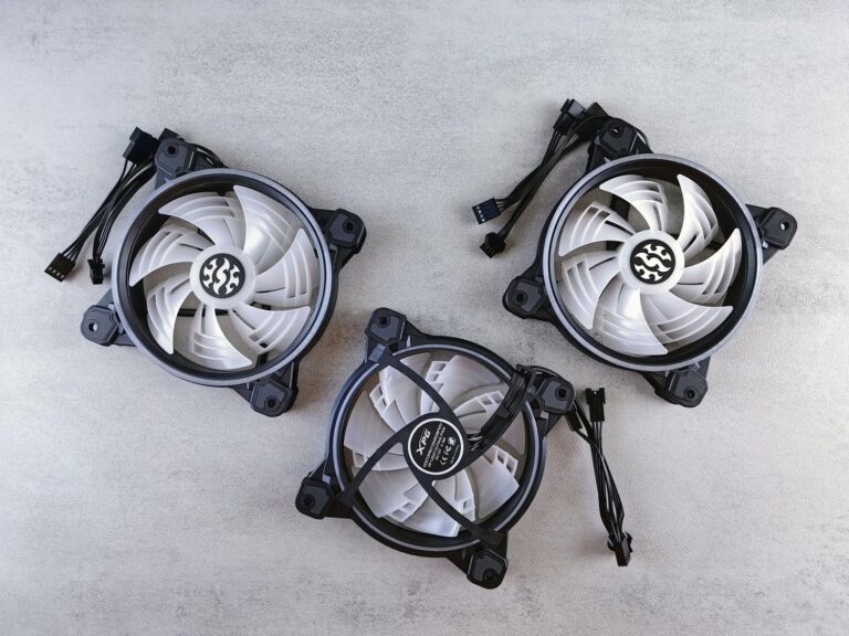 Tres ventiladores de refrigeración para PC con cables de conexión PWM y ARGB sobre un fondo gris neutro.