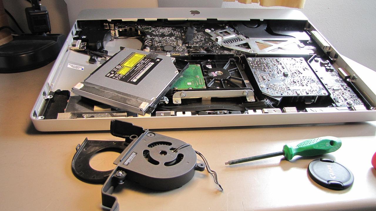 Proceso de reparación técnica de un iMac exponiendo los ventiladores internos y la placa lógica.