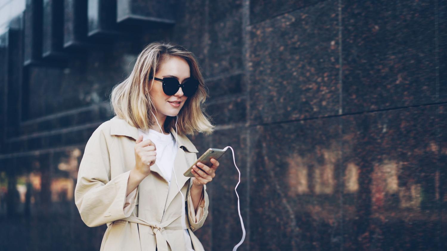 Mujer con estilo urbano utilizando su teléfono y auriculares para escuchar música al aire libre.