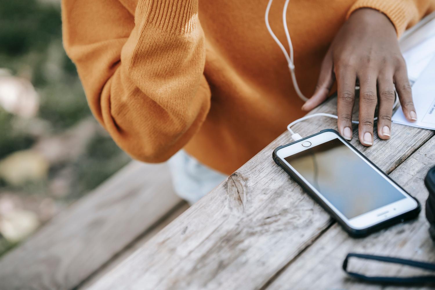 Vista cenital de una mujer usando su smartphone con auriculares para organizar su biblioteca musical.