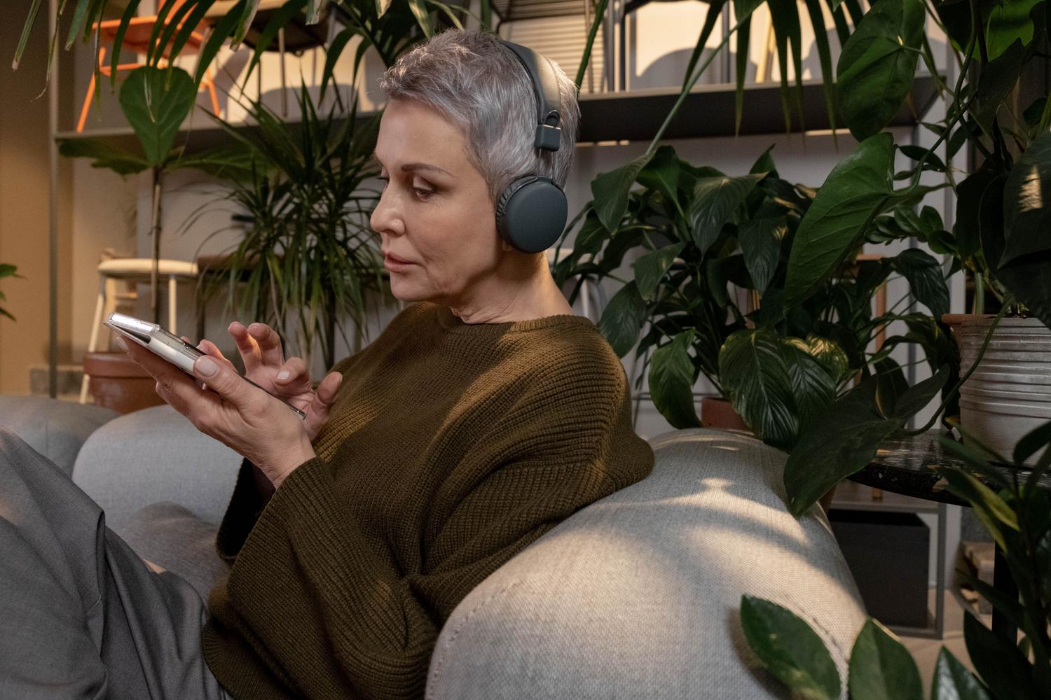 Mujer mayor en un salón acogedor gestionando su música en Spotify a través de su móvil y auriculares.