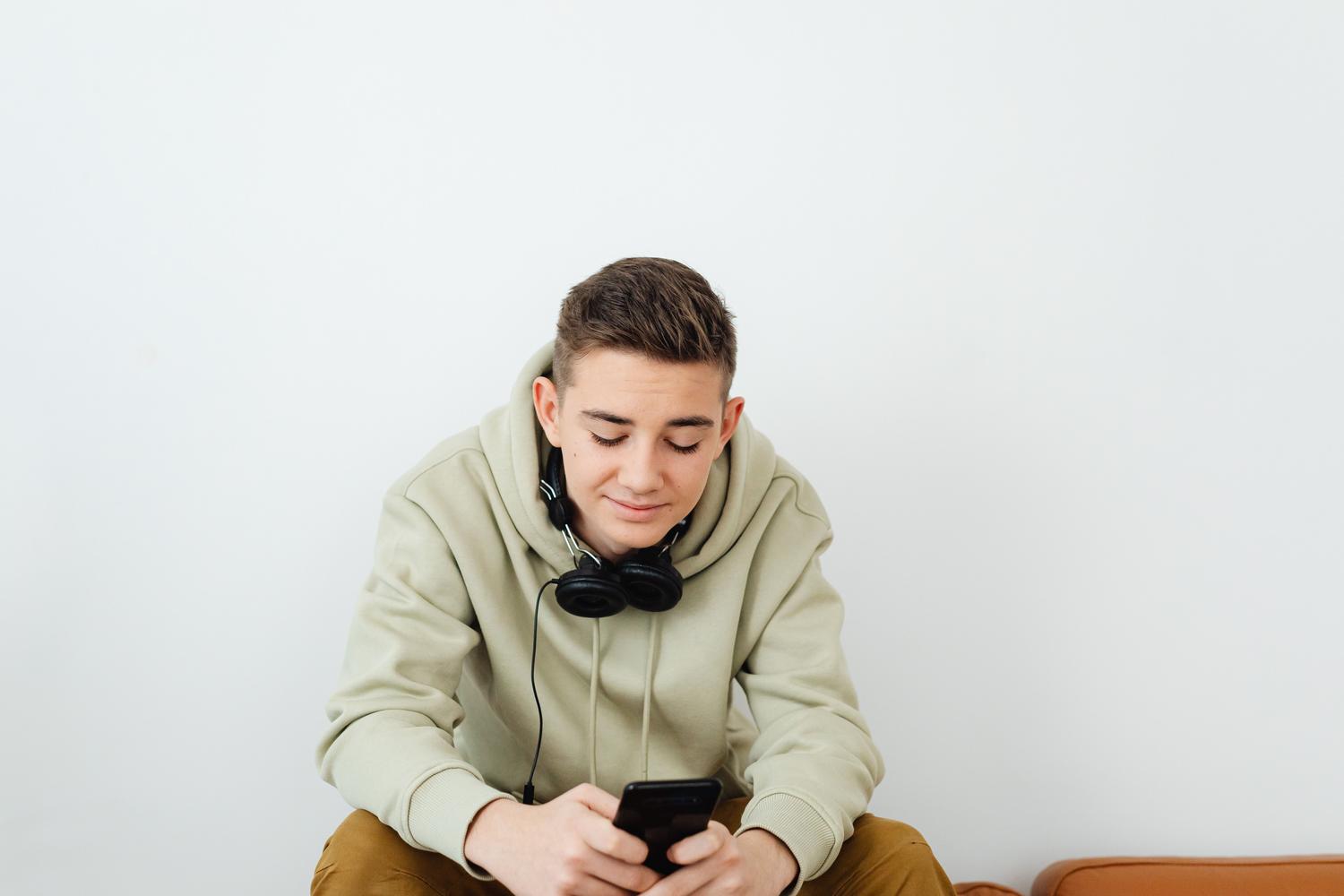 Joven con auriculares alrededor del cuello interactuando con la aplicación de música en su teléfono móvil.