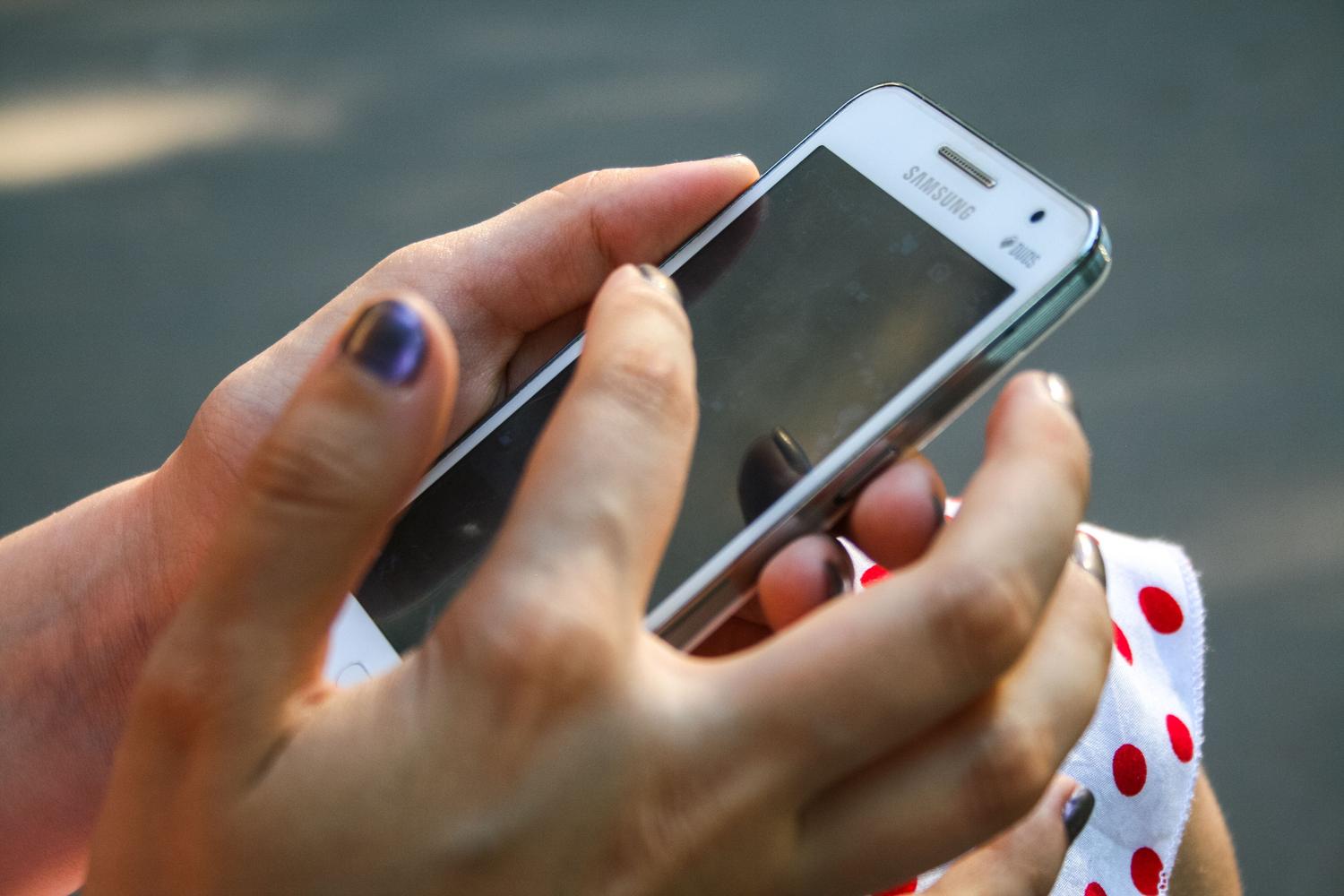 Persona sosteniendo un teléfono Samsung blanco en un entorno exterior, ilustrando la experiencia de usuario y el uso cotidiano del dispositivo.