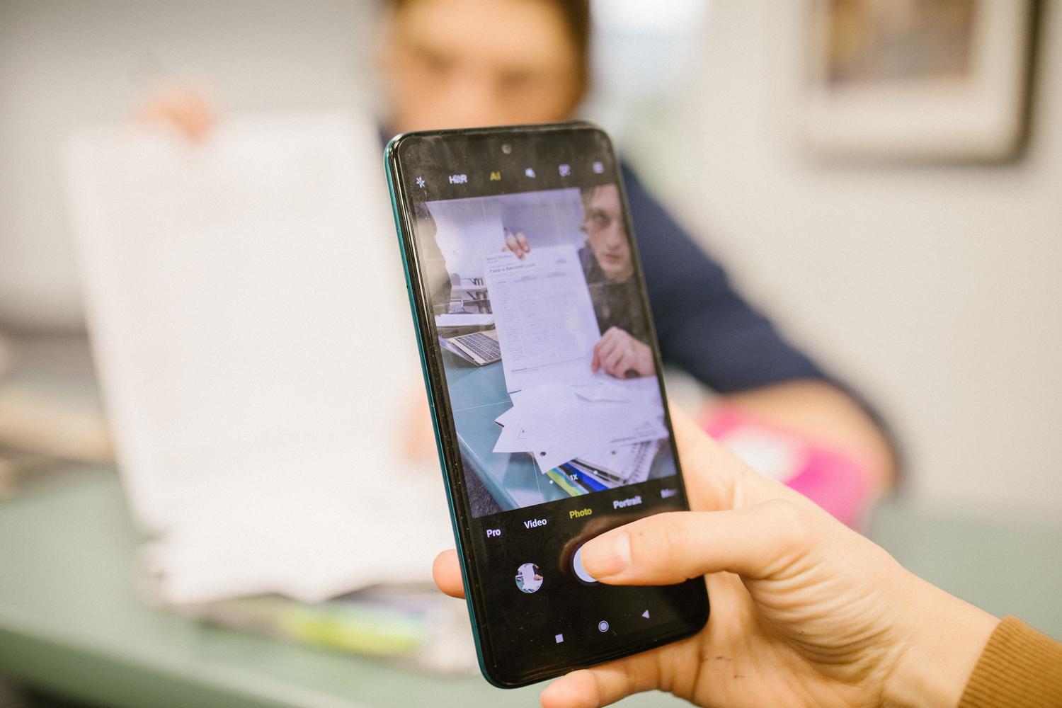 Primer plano de una persona utilizando la cámara de su smartphone para digitalizar un documento de papel sobre una mesa.