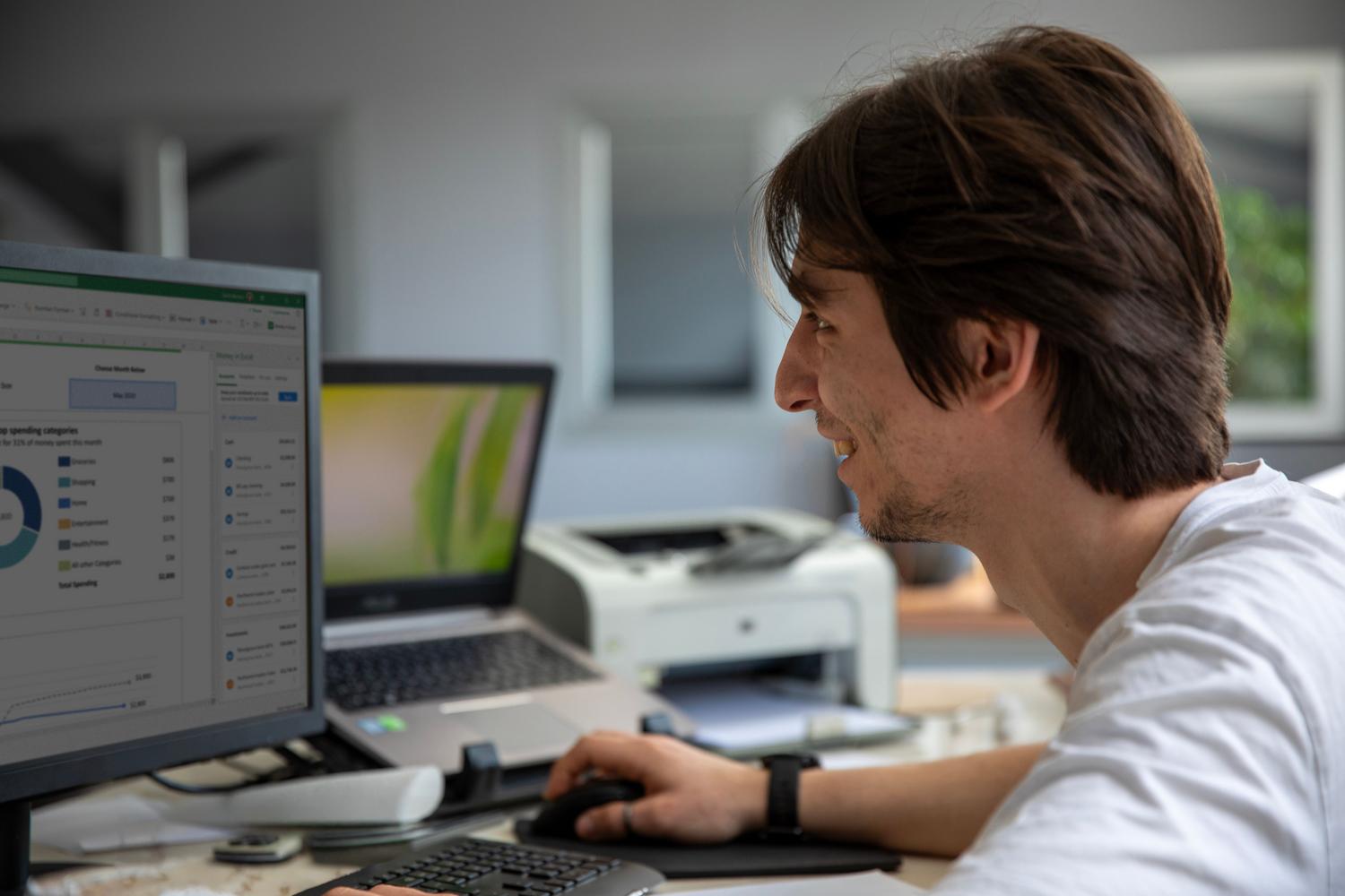 Un profesional sonriente trabajando en un ordenador en una oficina moderna, representando la eficiencia y facilidad que aporta la IA de Acrobat.