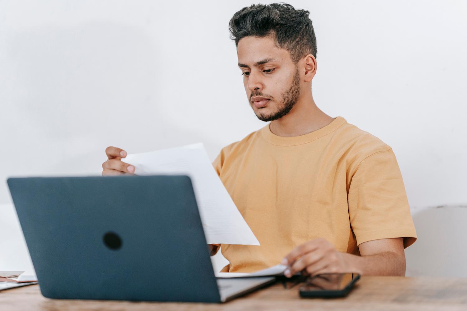 Estudiante concentrado leyendo un documento mientras estudia con su laptop en un entorno académico