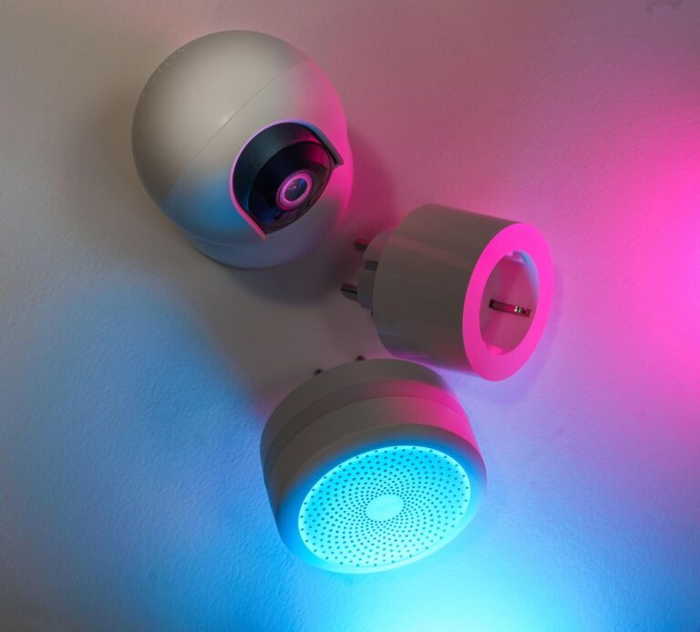 Dispositivos IoT inteligentes como cámaras y enchufes iluminados con luces neón azul y rosa, representando la conectividad moderna.