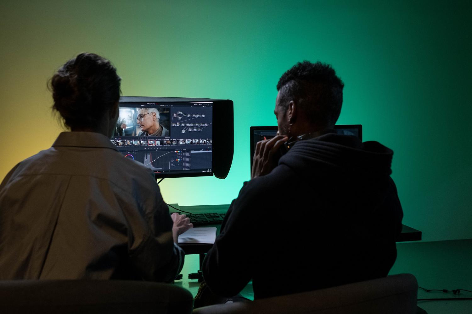 Dos profesionales creativos colaborando en un estudio profesional frente a un monitor con visera para garantizar la precisión del color.