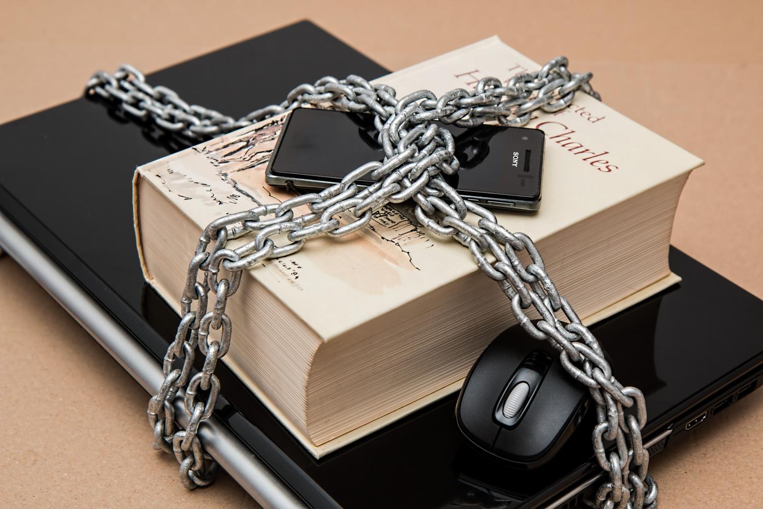 Dispositivos digitales y un libro encadenados, metáfora de la protección y seguridad de los datos personales.