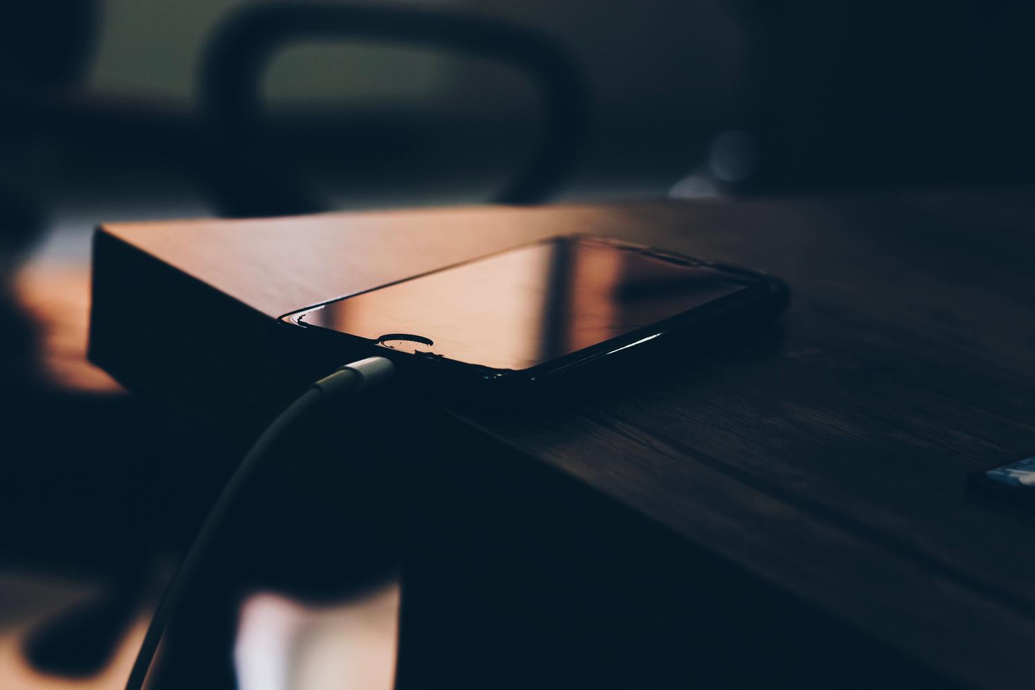 Smartphone connected to a charger on a wooden table, illustrating automatic background uploads.