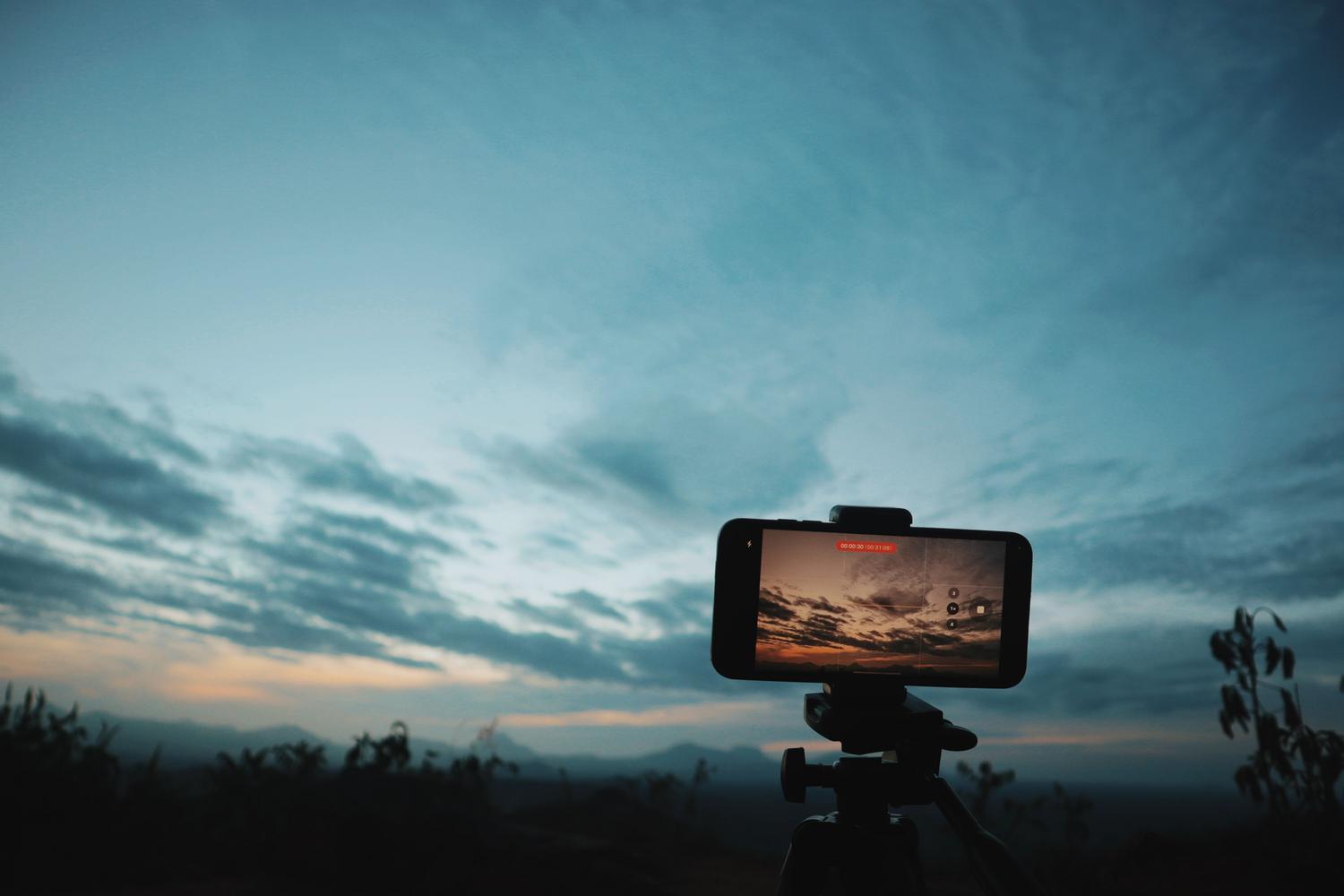 Smartphone on a tripod capturing a beautiful sunset, representing the act of creating digital memories.