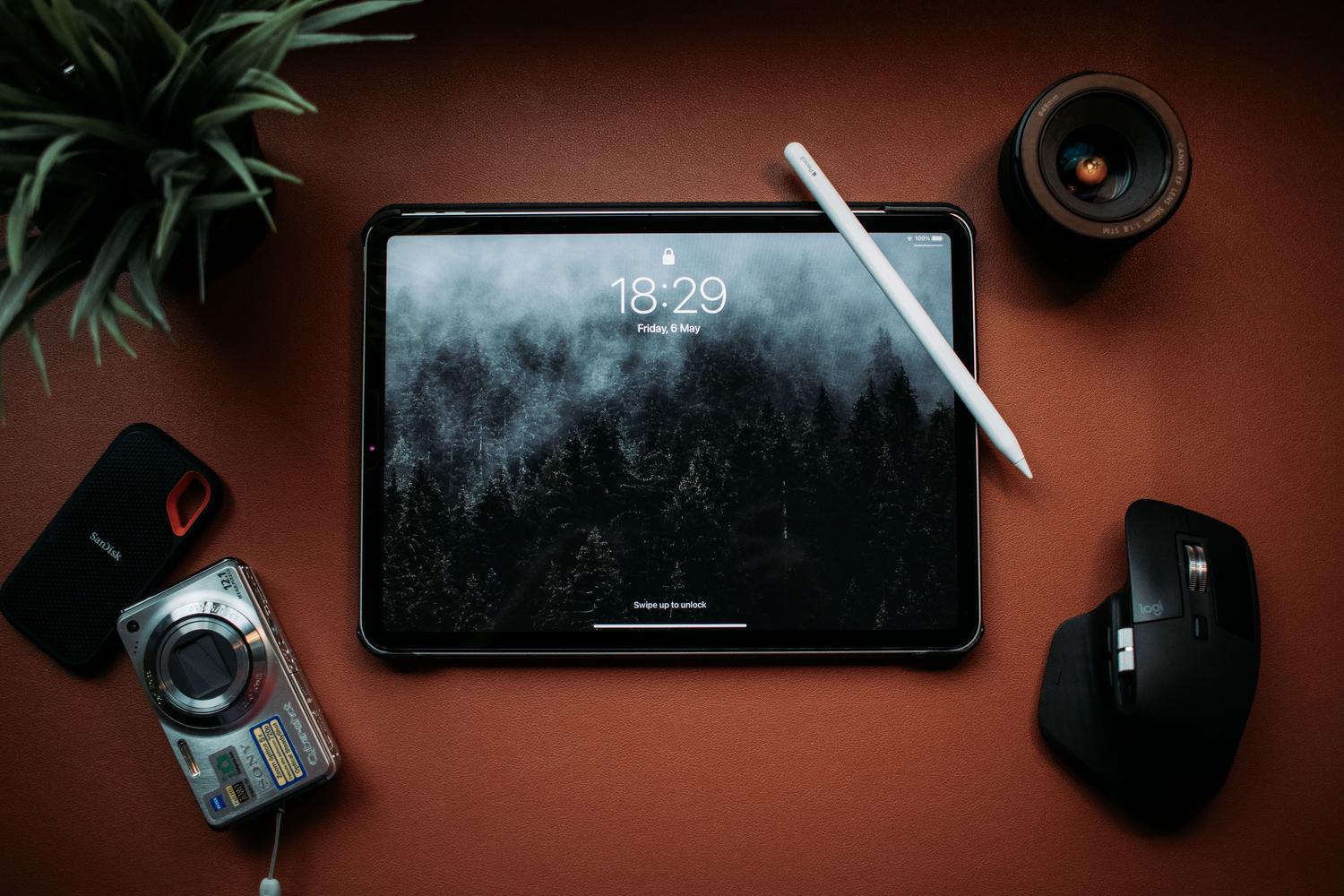 Flat lay de un iPad Pro con Apple Pencil y un SSD externo SanDisk sobre un escritorio de cuero, ideal para ilustrar la conexión entre tablet y almacenamiento externo.