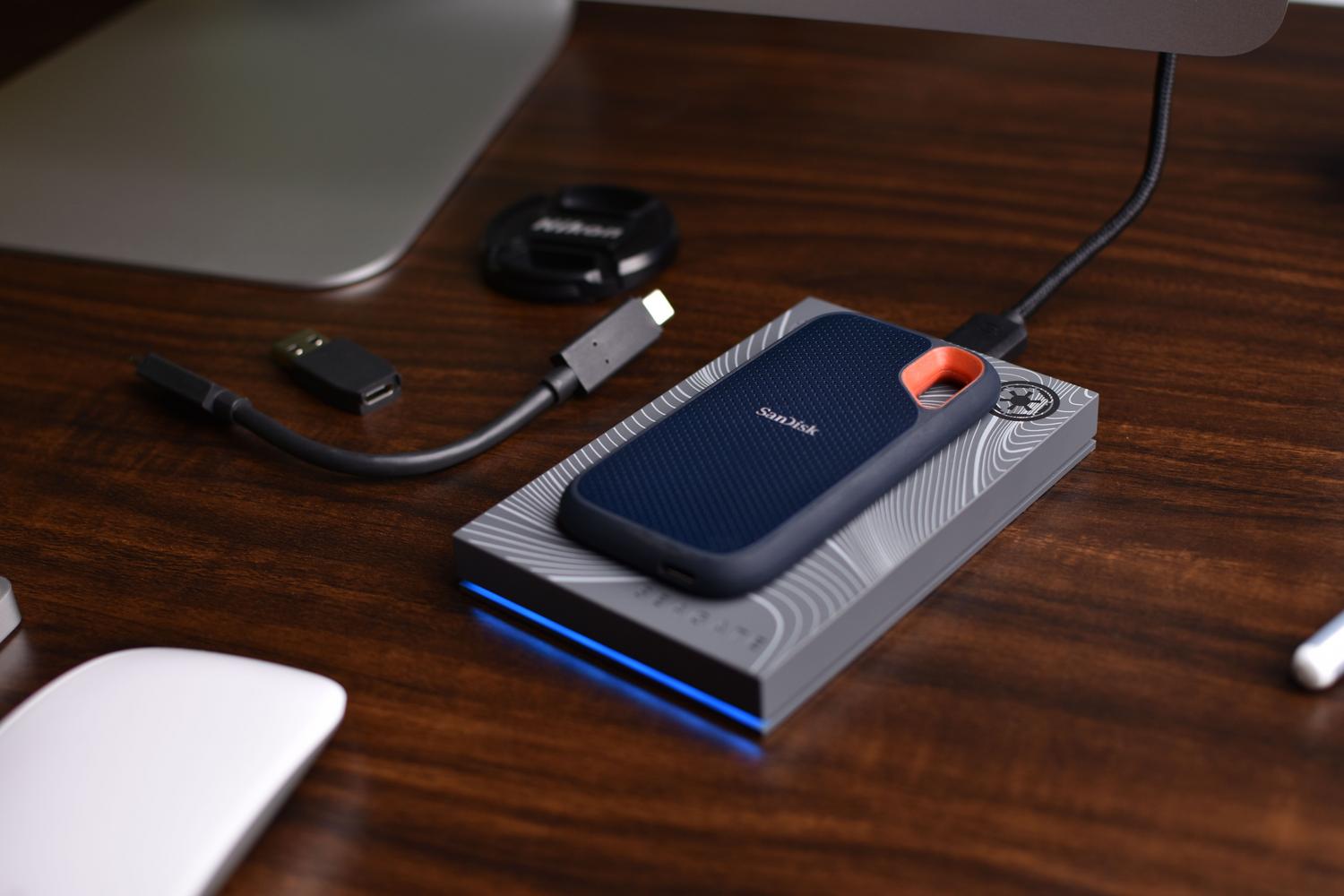 SSD portátil SanDisk sobre un escritorio de madera con accesorios USB, mostrando una solución de almacenamiento externo compacta.
