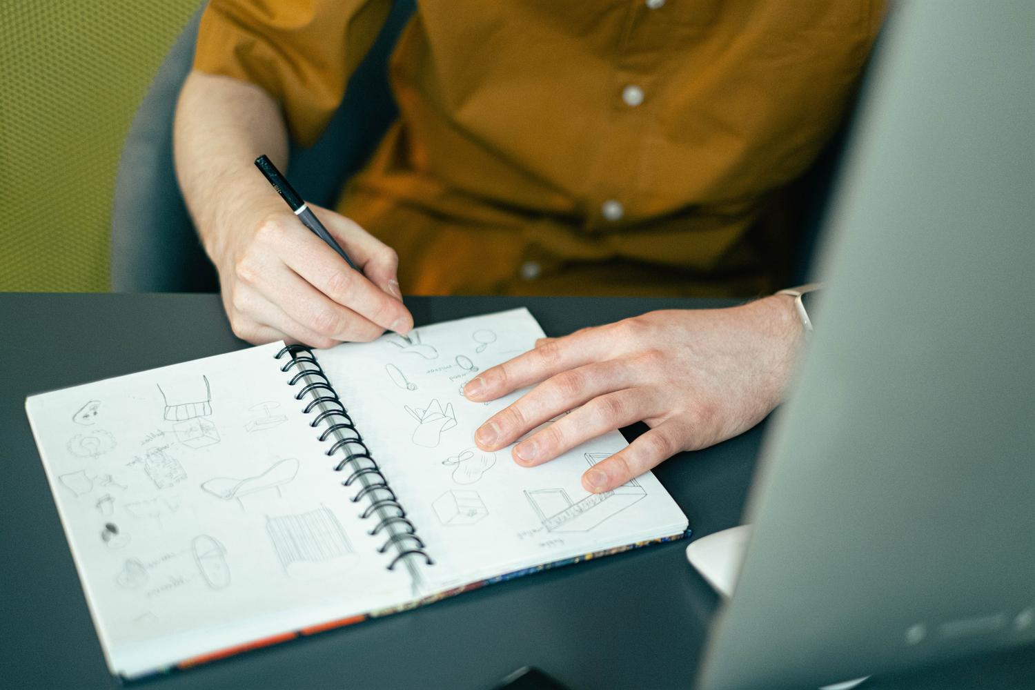 Diseñador bocetando ideas creativas en un cuaderno espiral como alternativa de planificación analógica