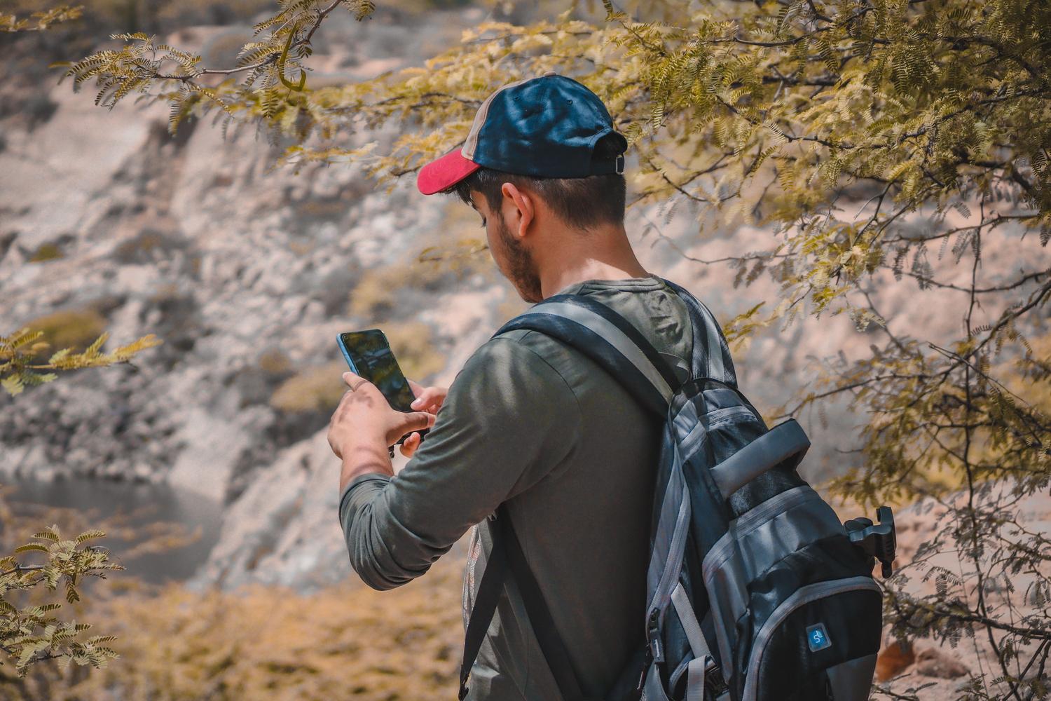 Hombre haciendo senderismo en un paisaje remoto consultando su móvil, ideal para ilustrar el uso de funciones sin conexión.