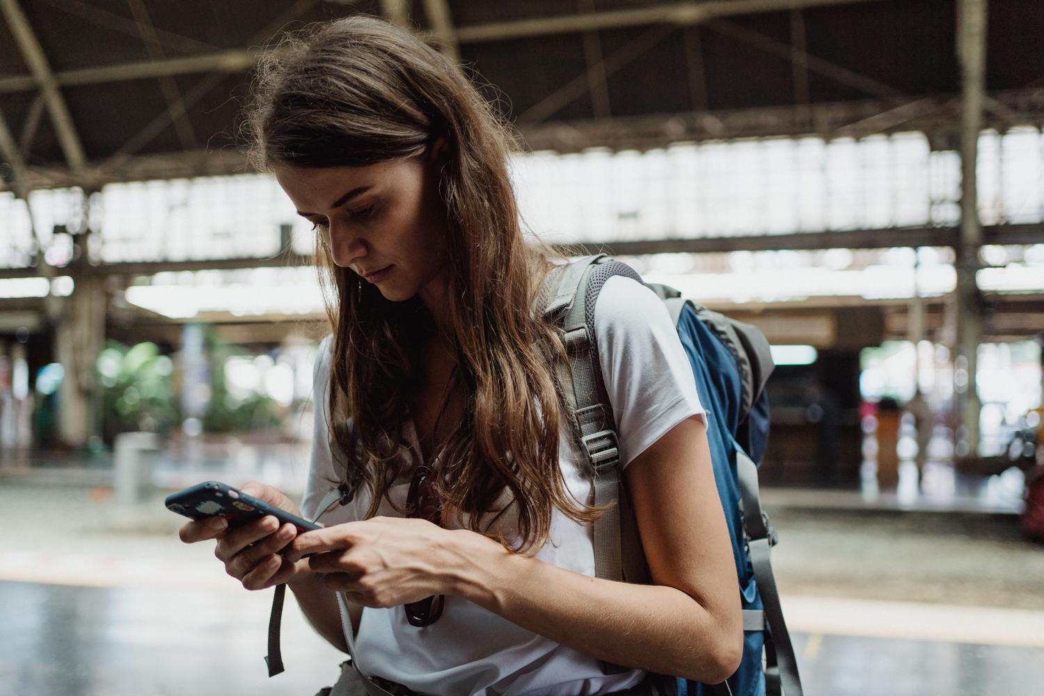 Mujer joven con mochila en una estación de tren utilizando su teléfono móvil para orientarse.