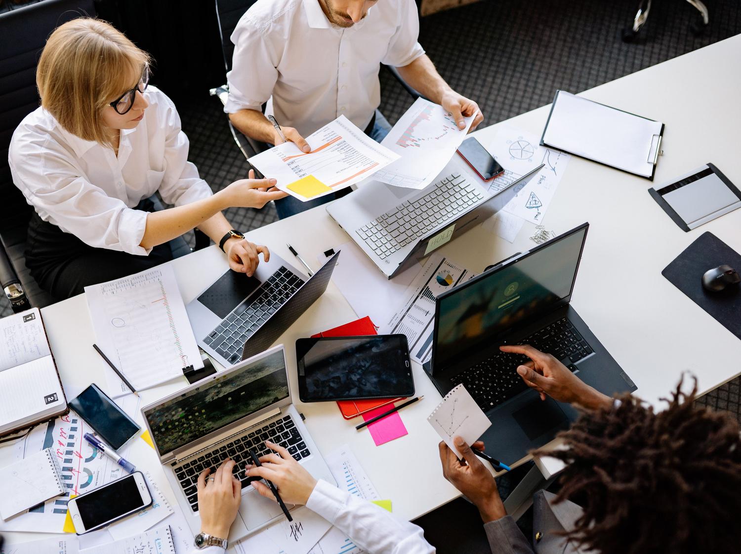 Vista cenital de un equipo diverso trabajando conjuntamente en un proyecto utilizando portátiles.
