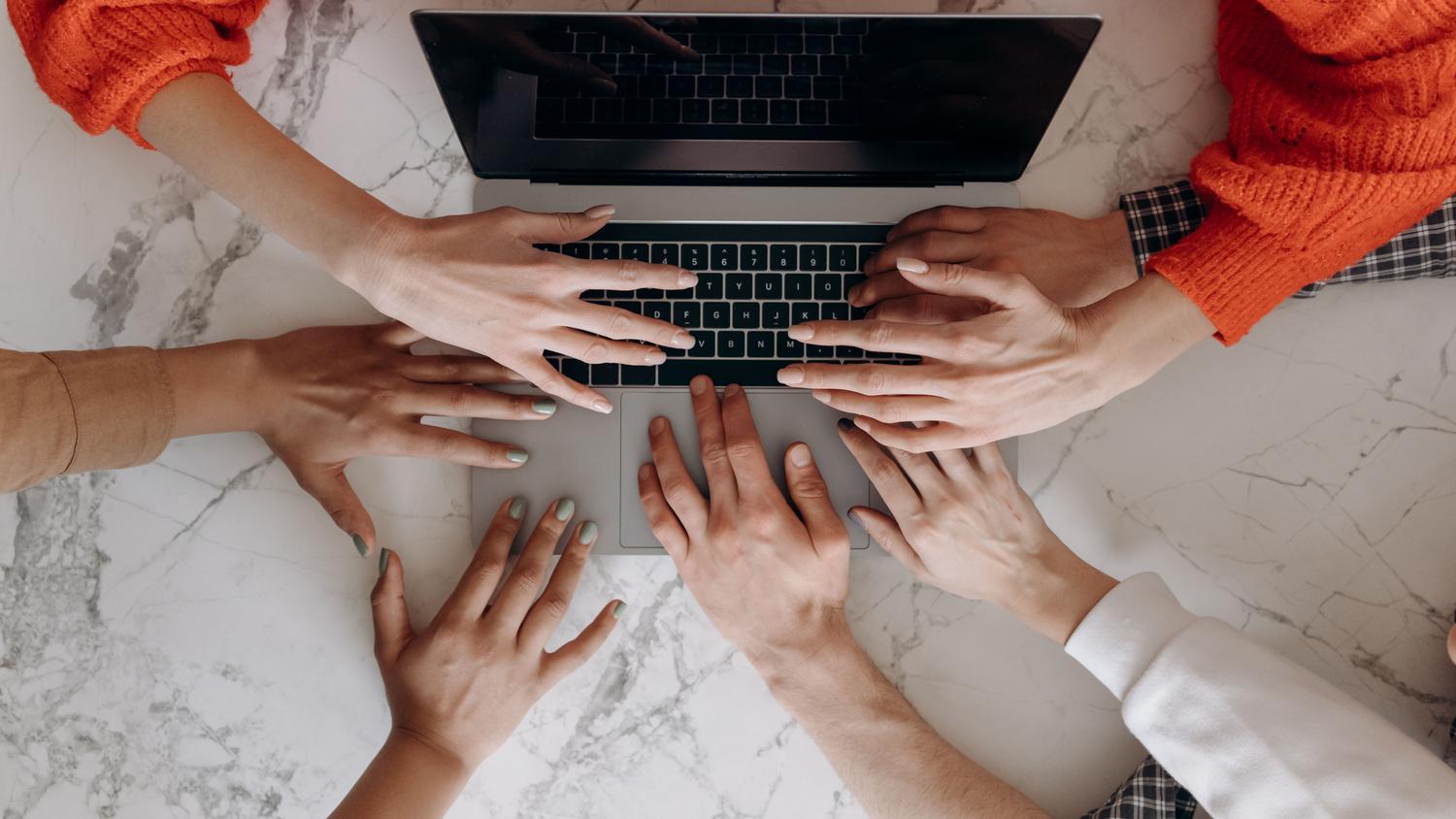 Vista cenital de un equipo diverso trabajando conjuntamente en un ordenador portátil, ilustrando la co-creación y el trabajo asincrónico de los componentes de Loop.