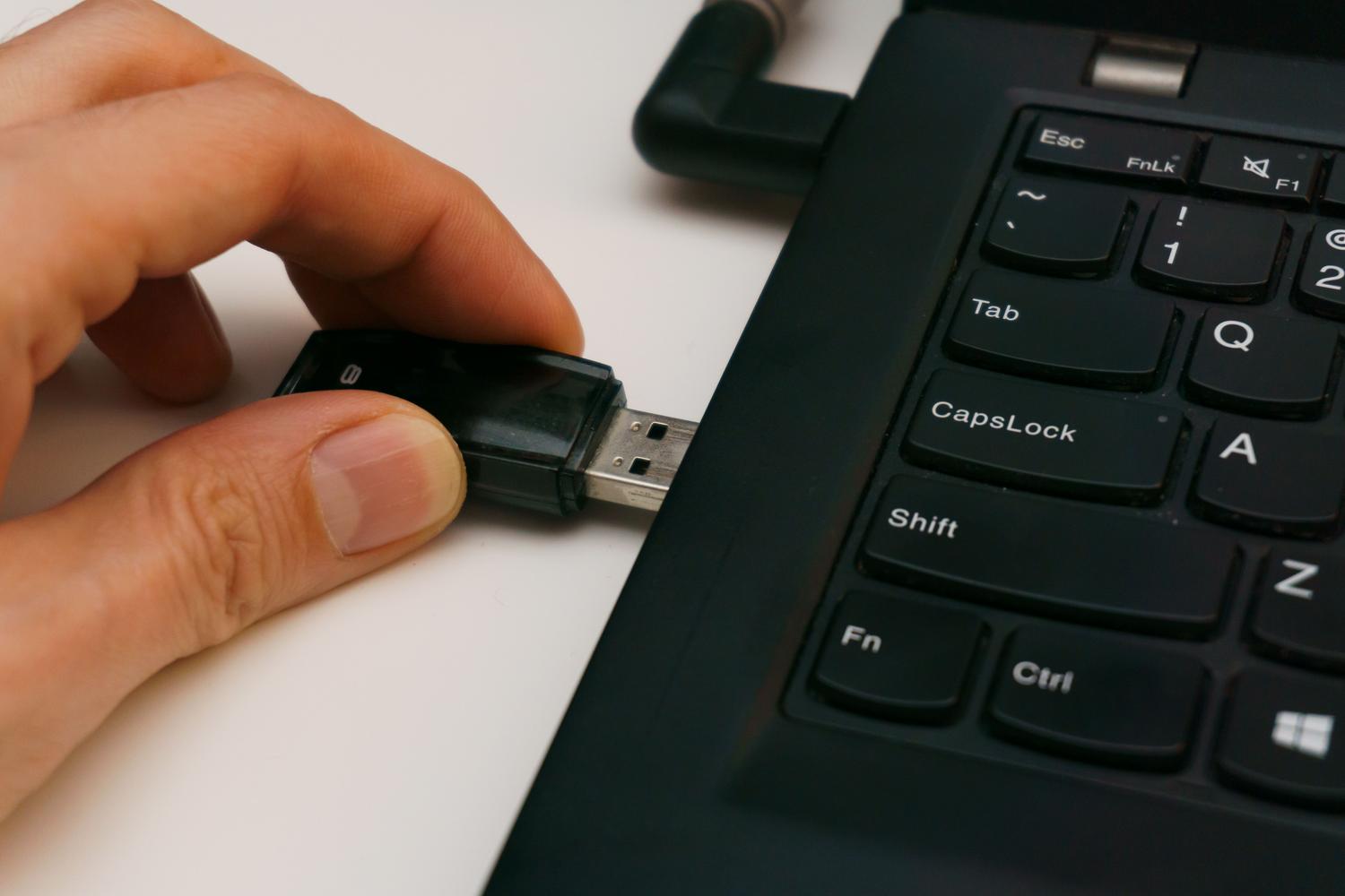 Primer plano de una mano insertando un pendrive USB negro en el puerto de un portátil.