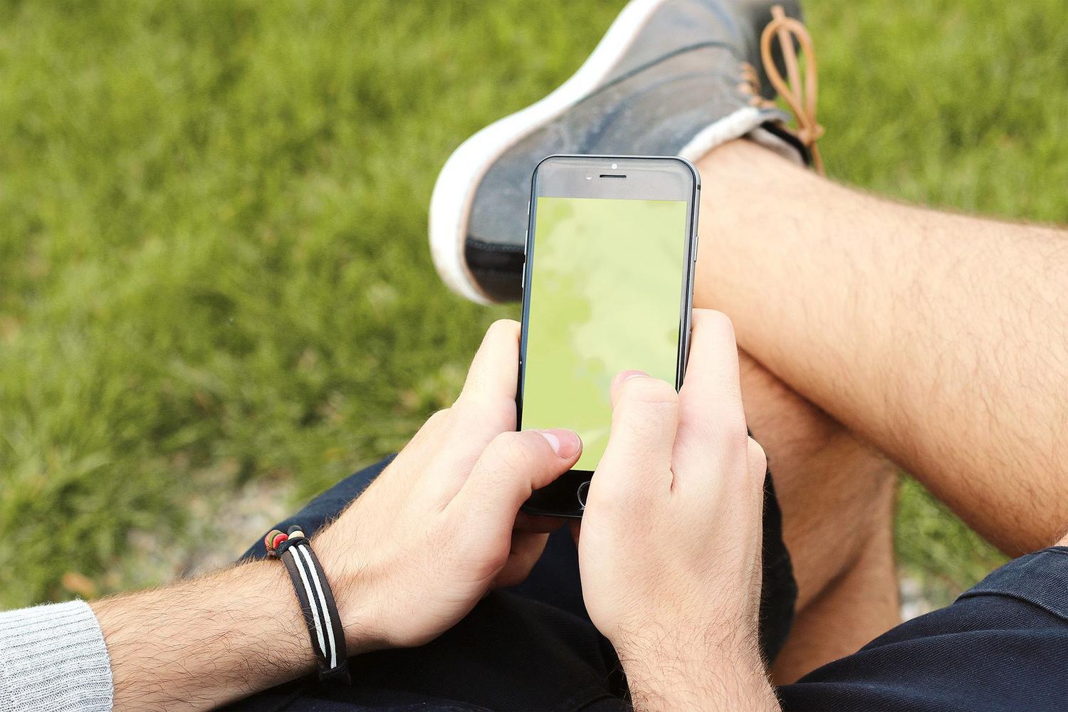 Primer plano de manos sosteniendo un smartphone con pantalla genérica en un entorno natural, representando el uso móvil cotidiano.