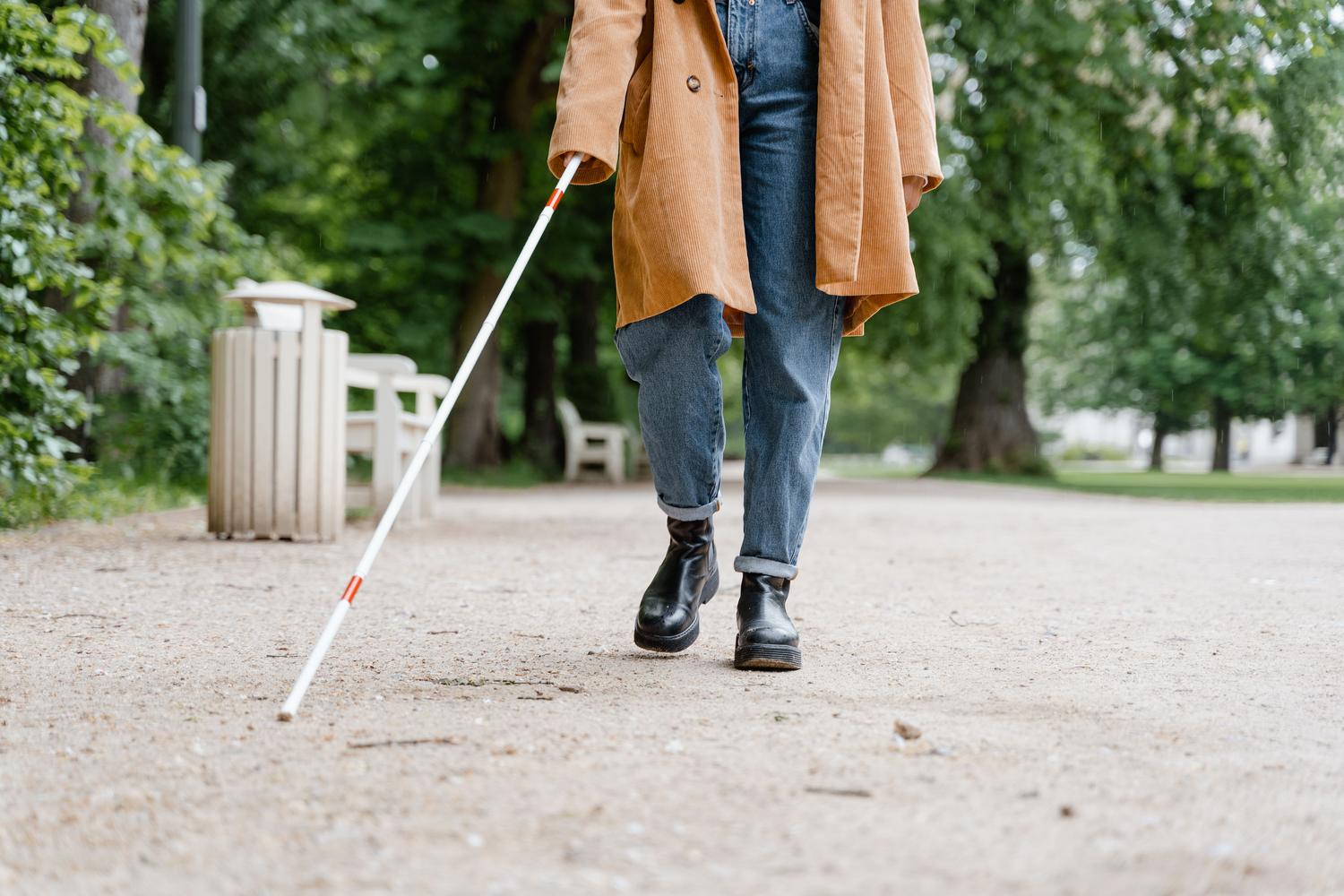 Una persona con discapacidad visual utilizando un bastón blanco para caminar por un parque, ilustrando la asistencia de Guided Vision de Gemini.