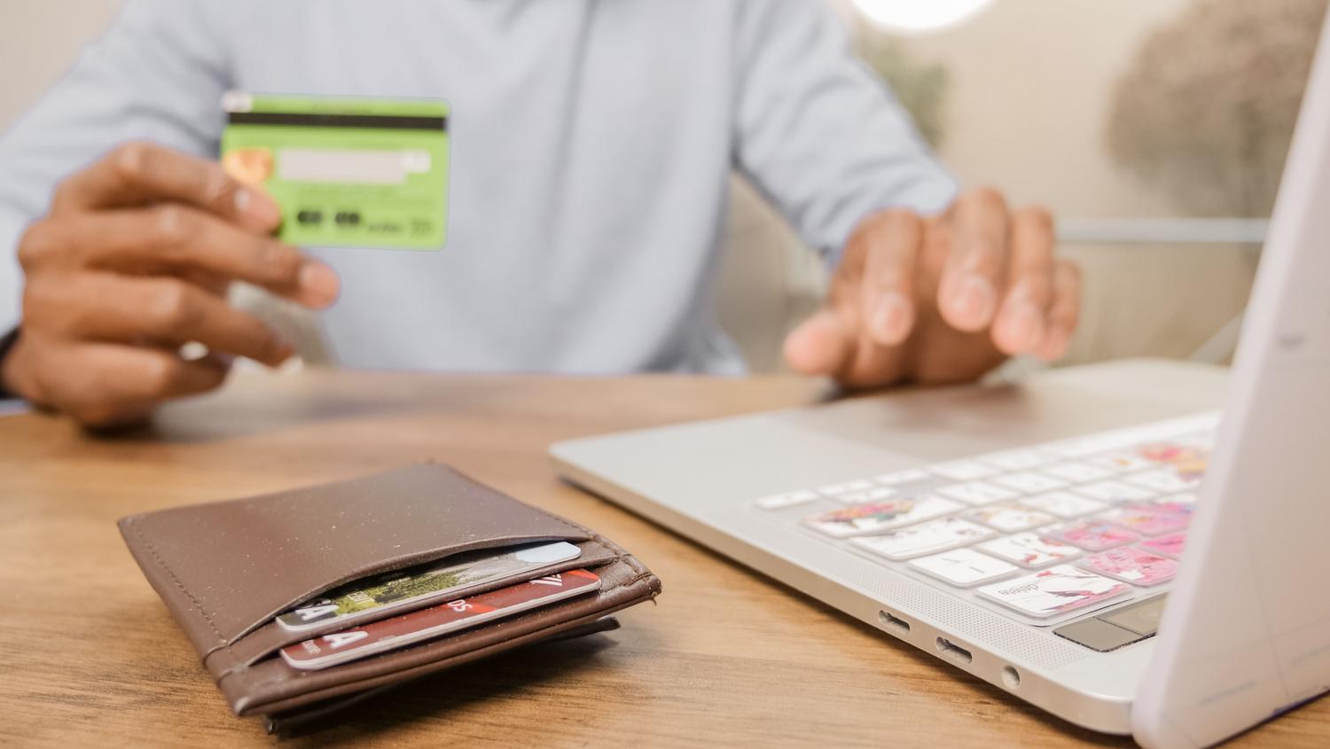 Persona utilizando un ordenador portátil y una tarjeta bancaria durante una compra por Internet.