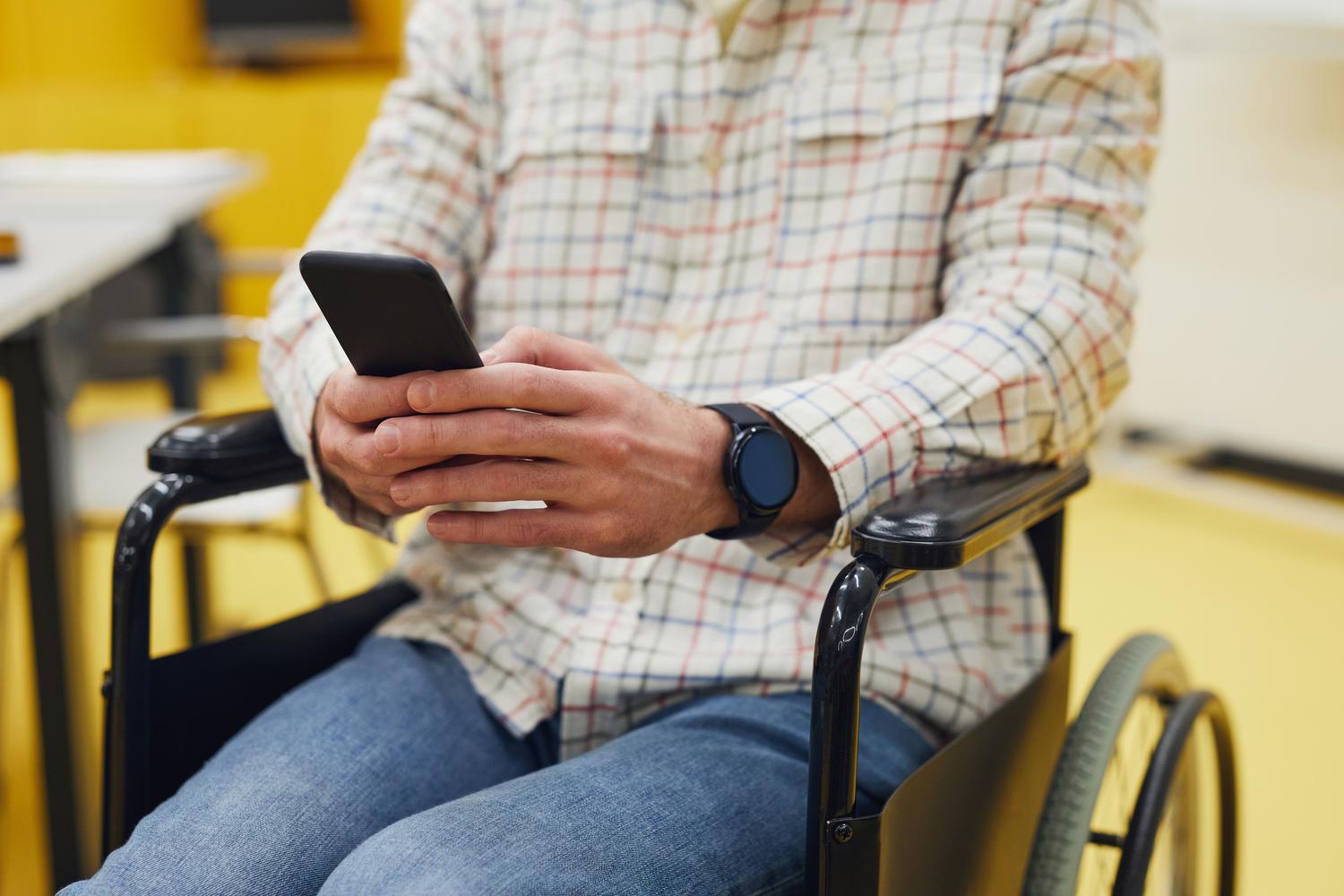 Persona en silla de ruedas utilizando un teléfono móvil, destacando la aplicación de la herramienta para mejorar la accesibilidad cotidiana.