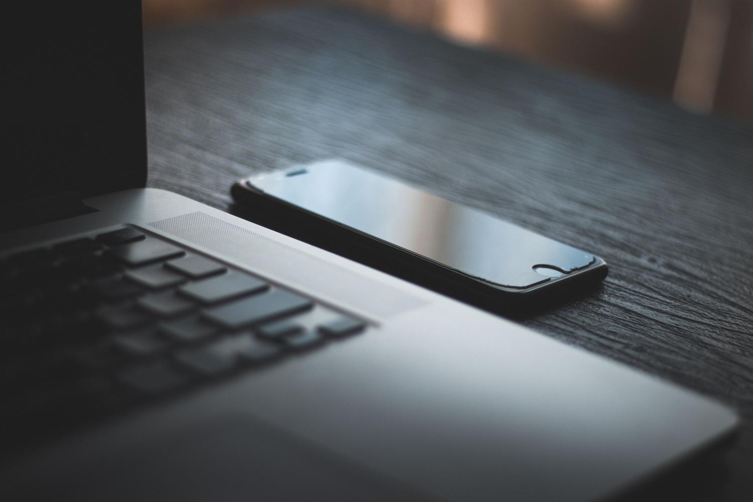 Smartphone y ordenador portátil sobre una mesa de madera, representando la integración entre dispositivos.